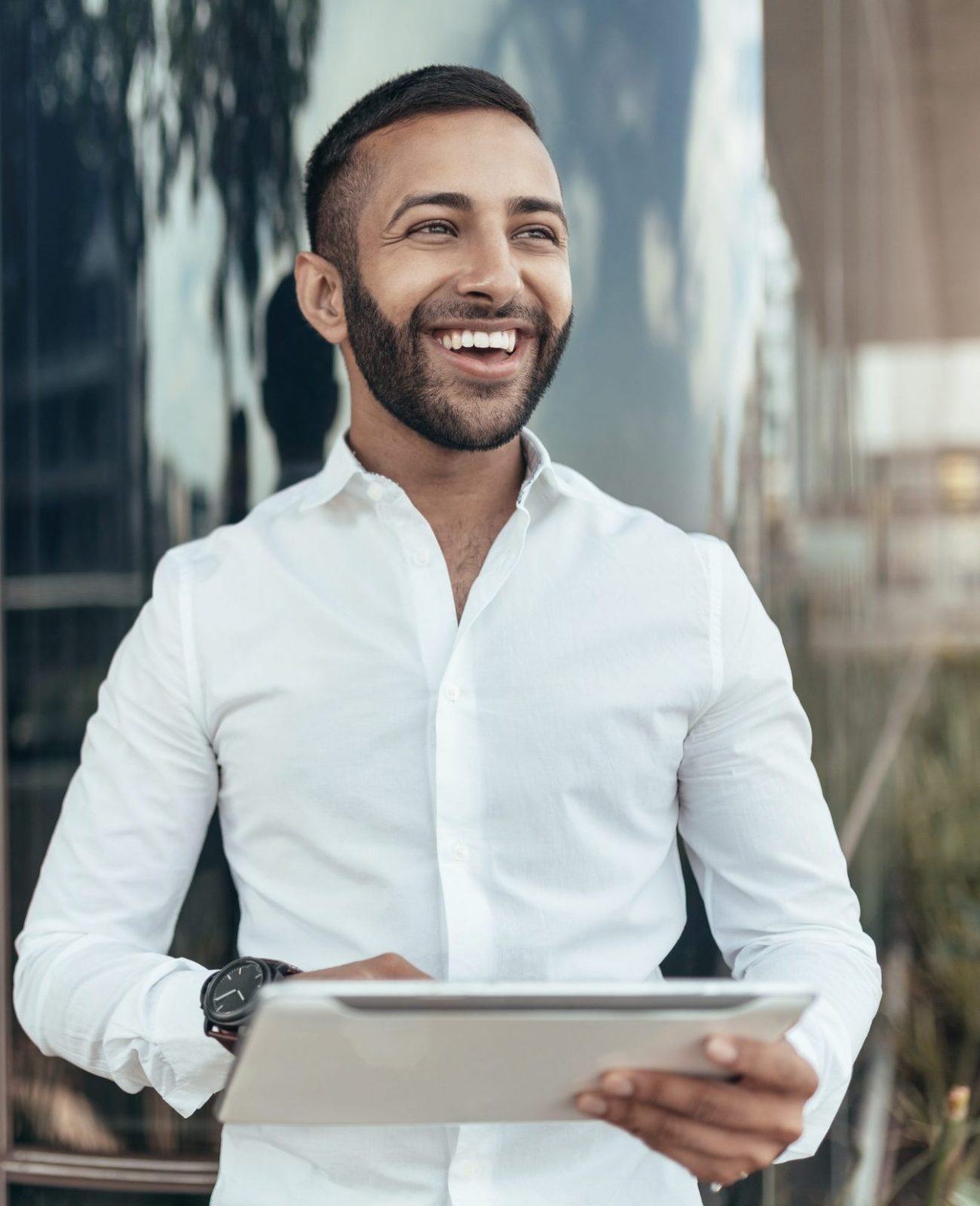 Portrait of a young confident smiling indian man holding a tablet and looking into the distance